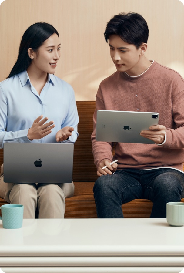 两位同事坐在沙发上,一位用 MacBook,一位用 iPad 与 Apple Pencil
