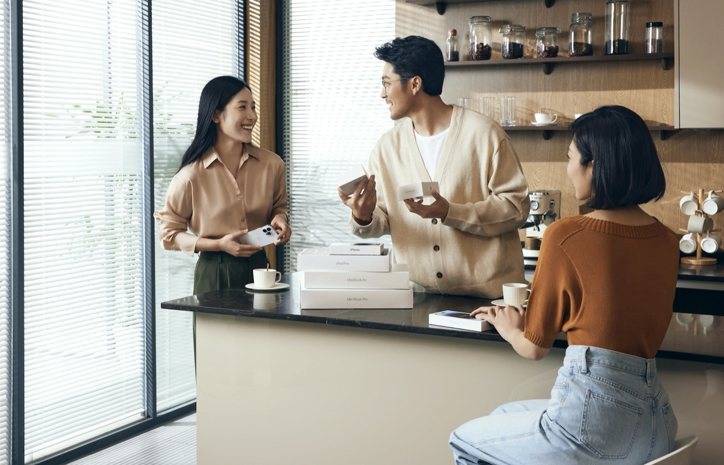 三位同事在办公室吧台前拆开 iPhone、iPad Pro 与 MacBook 的包装
